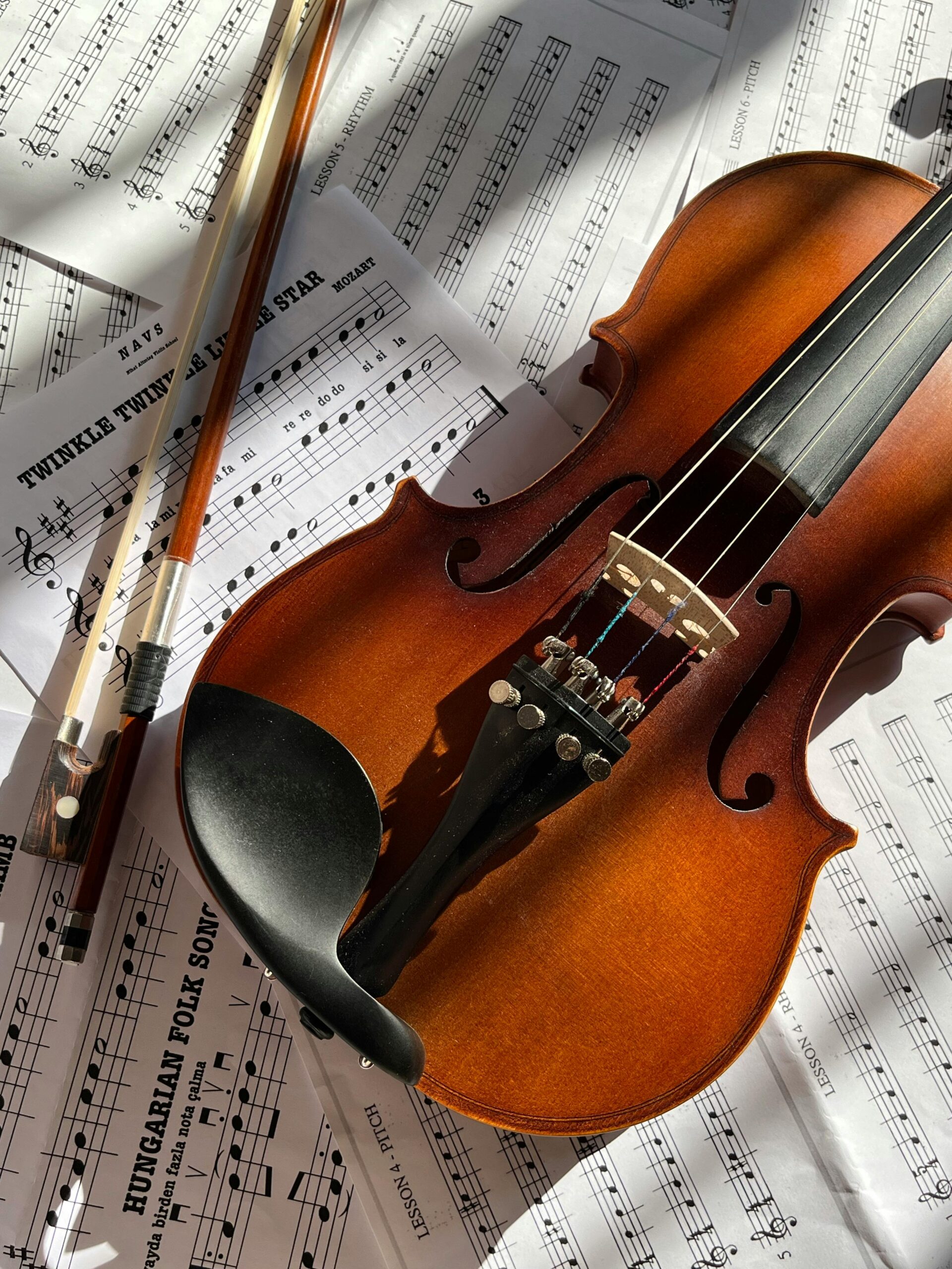 Close-up of a violin with bow on sheet music in warm sunlight.
